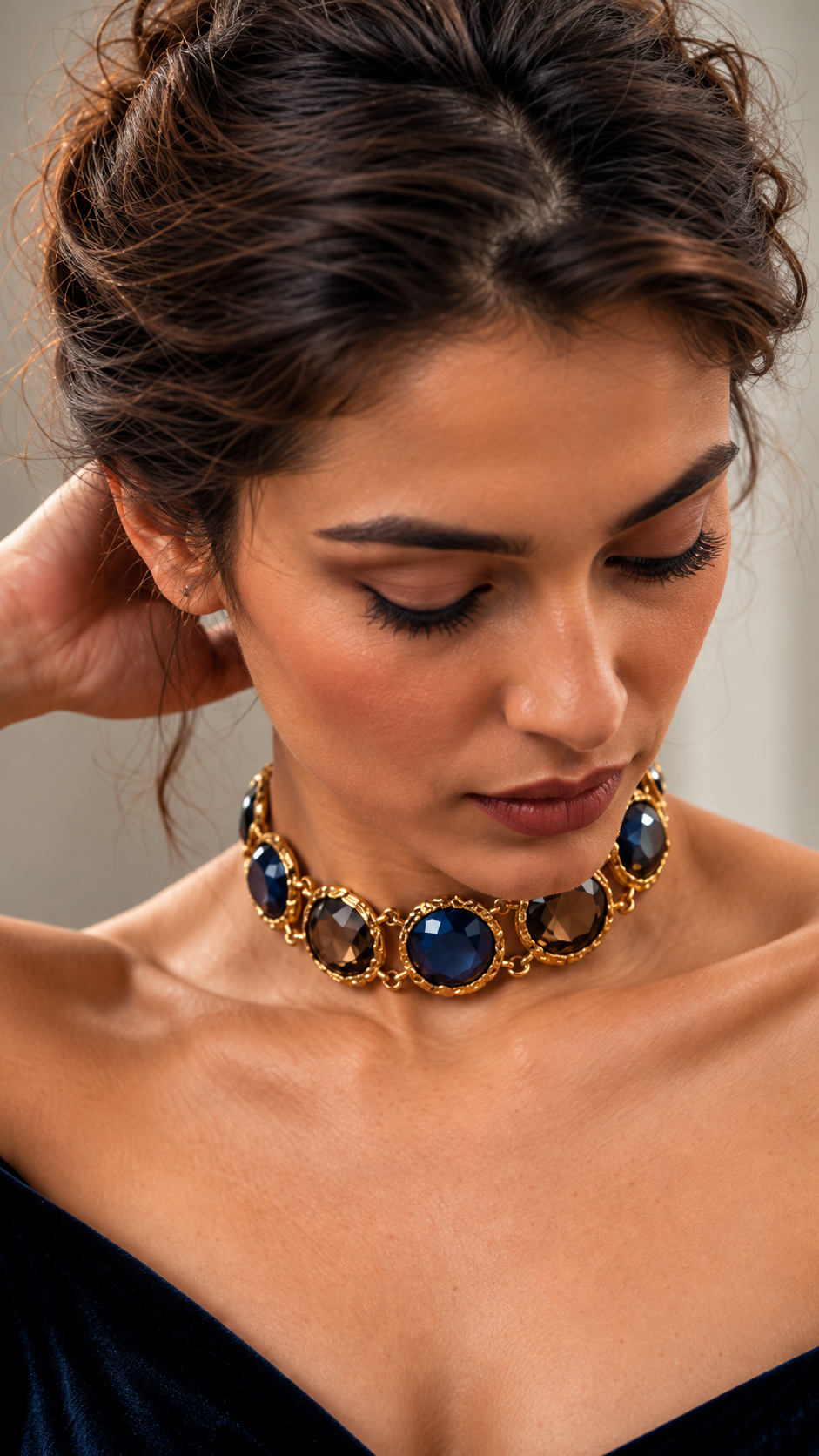 Model wearing a Medoso Jewellery antique gold-toned statement choker with alternating navy blue and smoky brown faceted gemstones, photographed in warm editorial lighting.