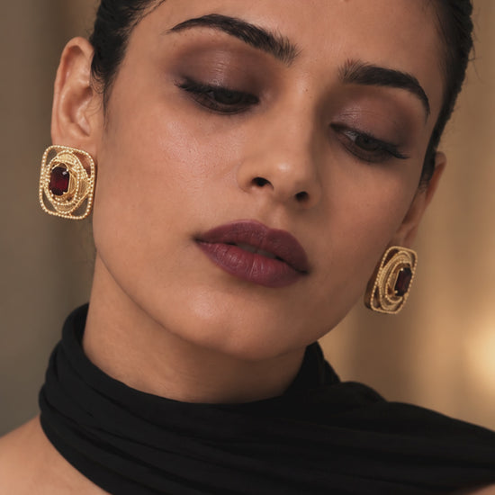 Rumaia Studs featuring a burgundy gemstone at the centre, framed by layered fluid geometric contours and delicate pavé detailing, blending heritage-inspired artistry with contemporary jewellery design.