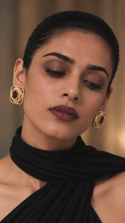 Rumaia Studs featuring a burgundy gemstone at the centre, framed by layered fluid geometric contours and delicate pavé detailing, blending heritage-inspired artistry with contemporary jewellery design.